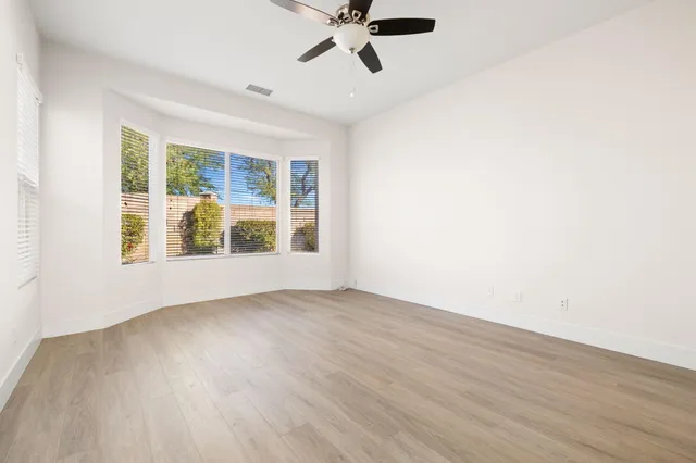 an empty room with wooden floor fan and windows