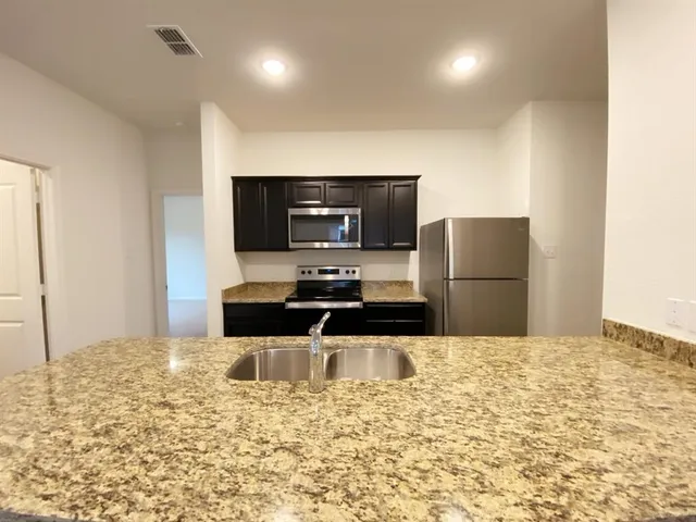 a view of kitchen with kitchen island granite countertop stainless steel appliances counter space and wooden floor