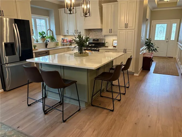 a kitchen with stainless steel appliances a dining table chairs a sink dishwasher and a refrigerator with wooden floor