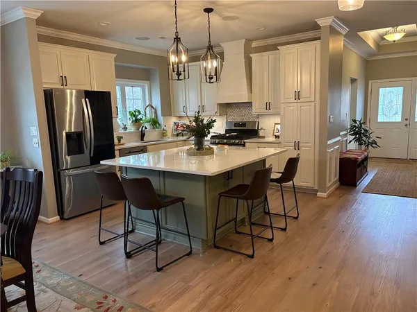 a kitchen with stainless steel appliances granite countertop a dining table chairs refrigerator and sink