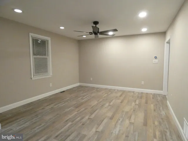 an empty room with wooden floor ceiling fan and window