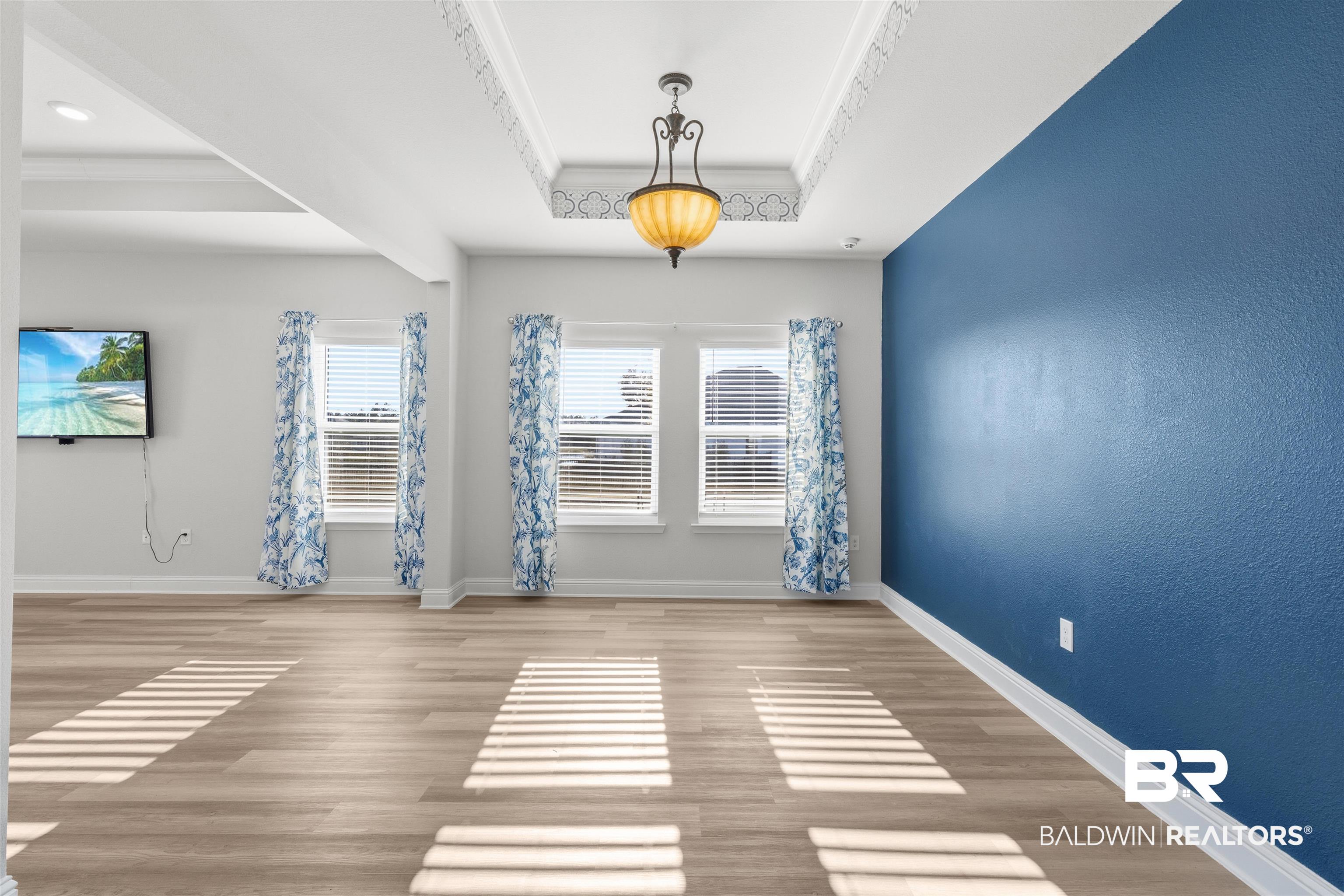 485 Shepard Street Gulf Shores, AL 36542 - Photo 11 of 53 Empty room featuring light wood-style floors, a tray ceiling, crown molding, and a textured wall