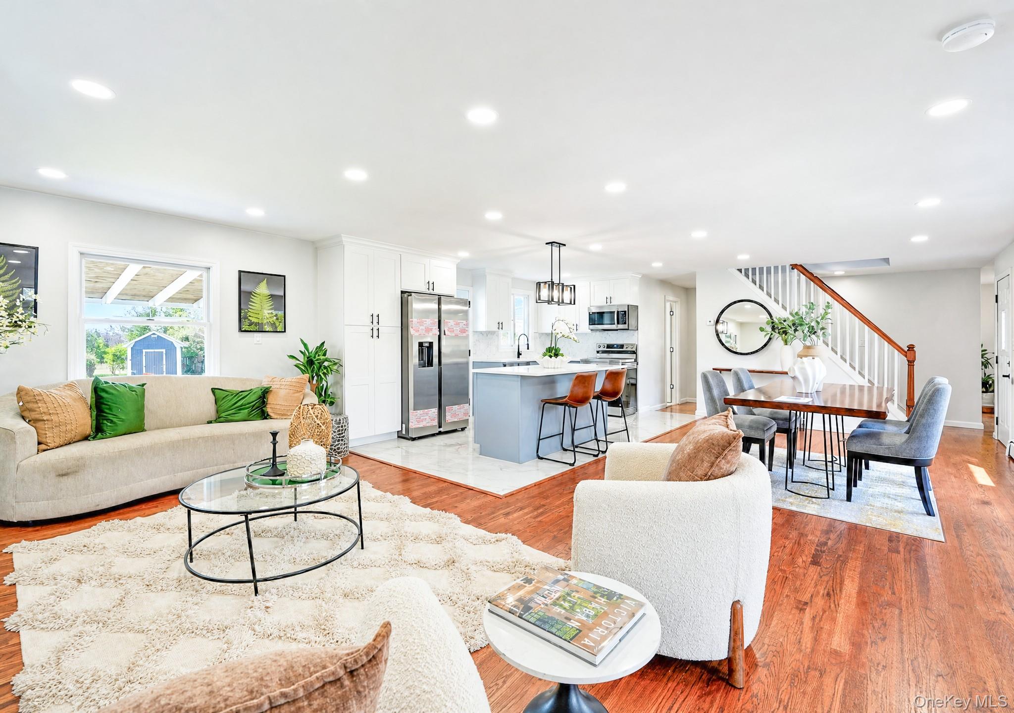 61 Cheshire Road Bethpage, NY 11714 - Photo 5 of 25 Open-concept living space featuring hardwood flooring, recessed lighting, a modern kitchen island with seating, white shaker cabinetry, and stainless steel appliances