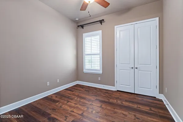 a view of an empty room with chandelier fan and wooden floor