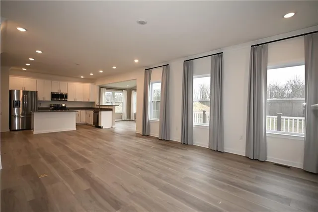 a view of an empty room with wooden floor and a kitchen