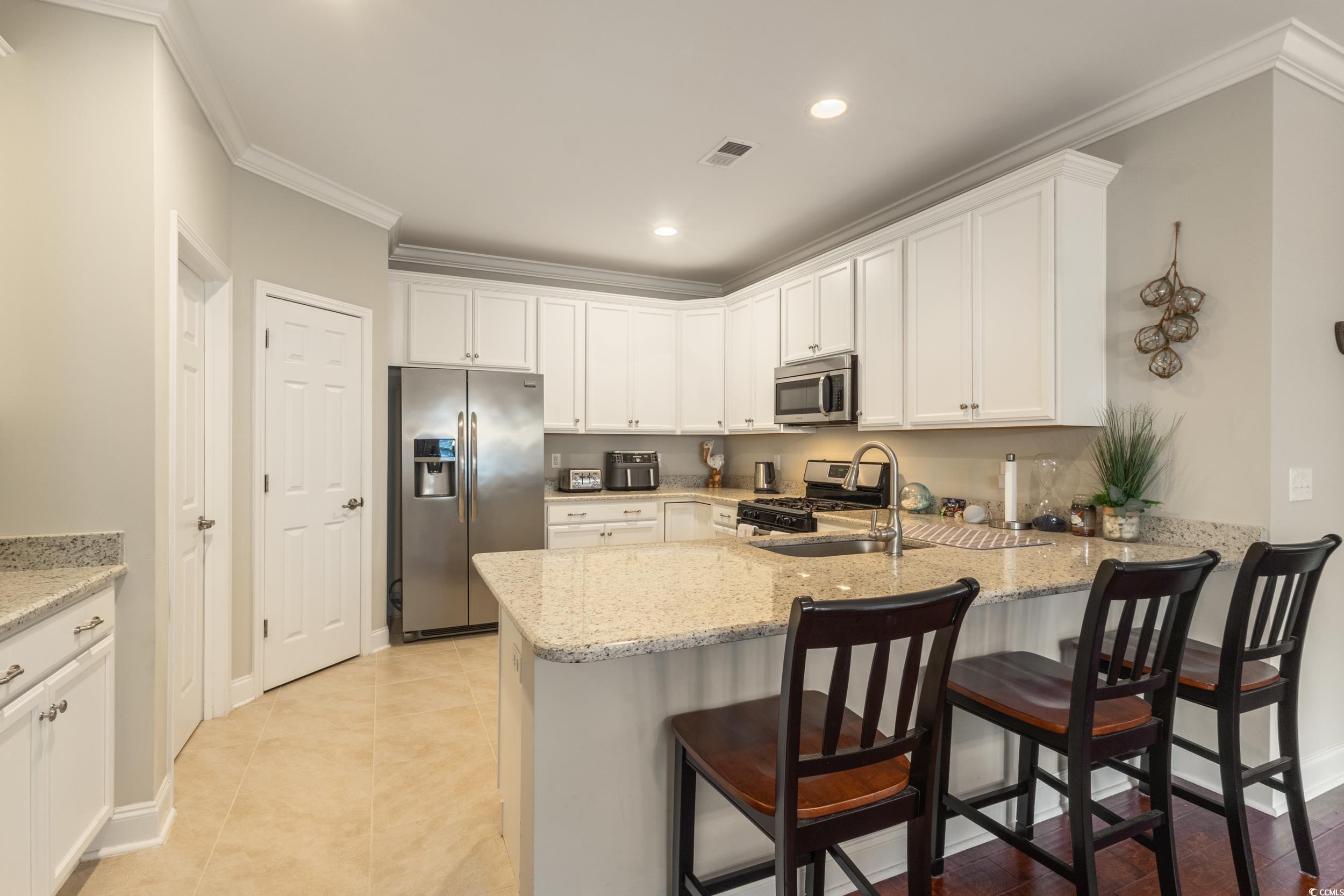 482 Botany Loop, Unit 155 Murrells Inlet, SC 29576 - Photo 11 of 40 Kitchen featuring white cabinets, stainless steel appliances, crown molding, light stone countertops, and a breakfast bar