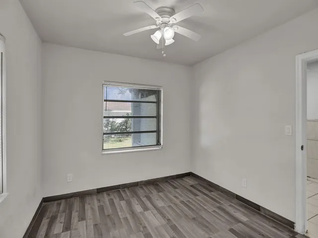 an empty room with wooden floor chandelier fan and windows