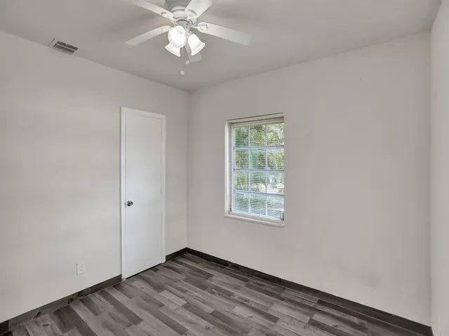 an empty room with wooden floor chandelier fan and windows