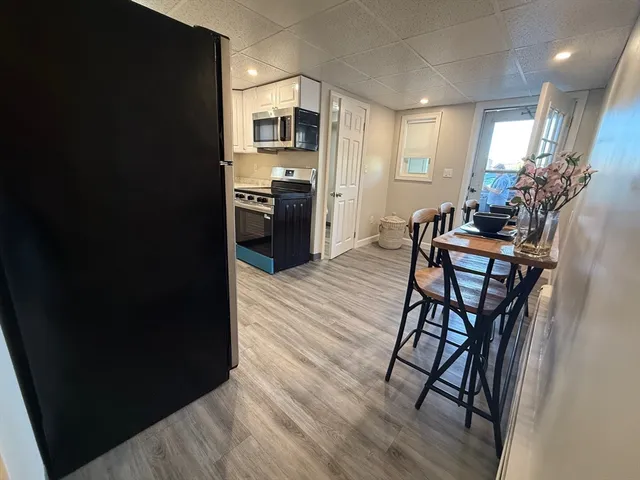 a kitchen with stainless steel appliances kitchen island granite countertop a refrigerator a stove a sink a dining table and chairs with wooden floor