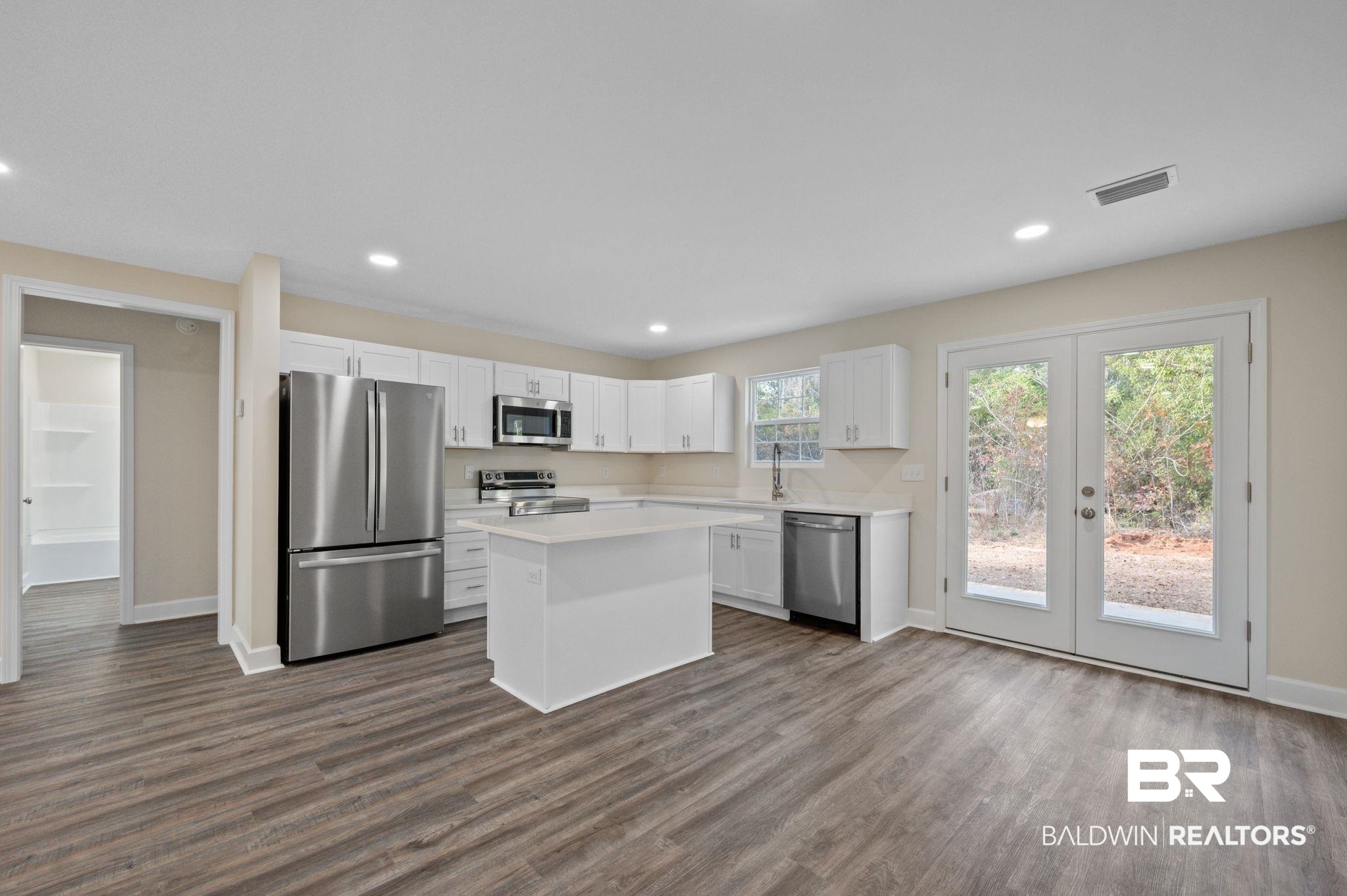1473 Pollard Road Daphne, AL 36526 - Photo 11 of 32 Kitchen with appliances with stainless steel finishes, dark hardwood / wood-style floors, white cabinets, a center island, and french doors