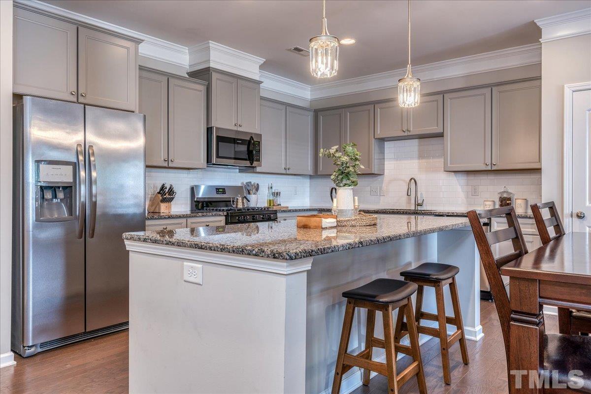 6328 Grace Lily Drive Raleigh, NC 27607 - Photo 3 of 27 a kitchen with stainless steel appliances granite countertop a stove a refrigerator a sink a dining table and chairs with wooden floor