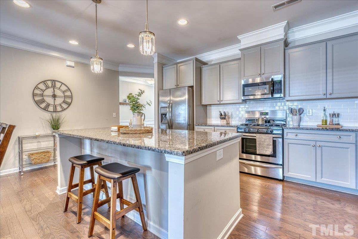 6328 Grace Lily Drive Raleigh, NC 27607 - Photo 9 of 27 a kitchen with kitchen island granite countertop wooden floors and cabinets