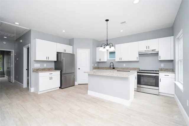 a kitchen with stainless steel appliances white cabinets a sink a stove a refrigerator and white cabinets