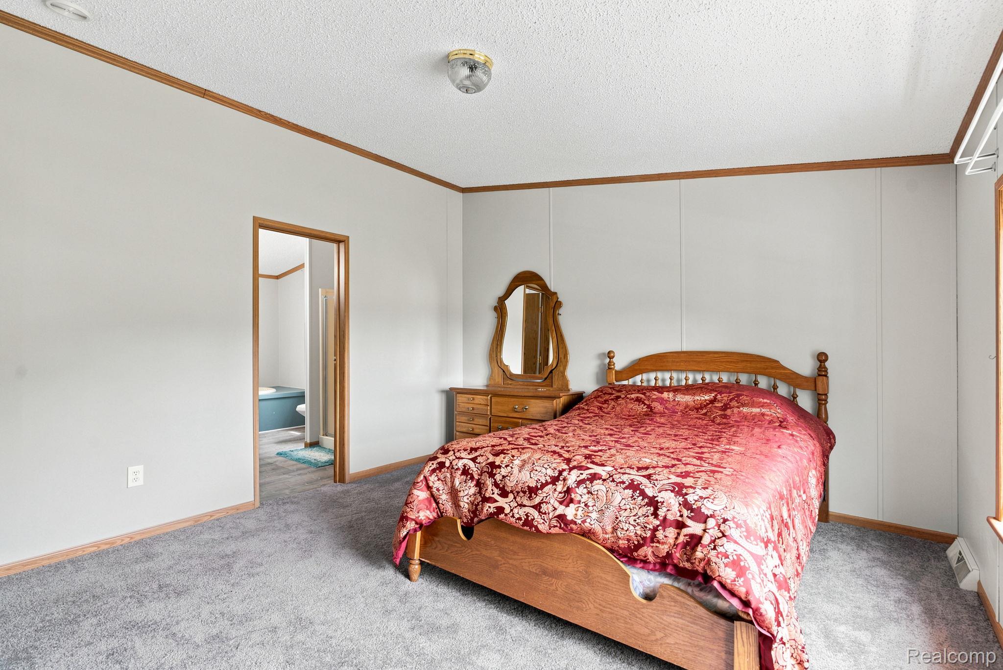 2390 Lakeshore Road Applegate, MI 48401 - Photo 23 of 97 Spacious primary bedroom featuring hardwood bed frame, large dresser with mirror, carpeted flooring, wood-trimmed ceiling detail, and abundant natural light from multiple windows