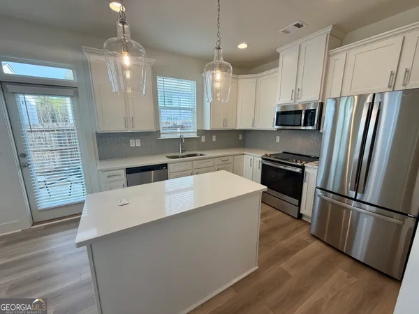 a large kitchen with stainless steel appliances a refrigerator a stove a sink dishwasher a oven and a dining table with wooden floor