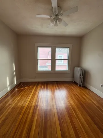 a view of an empty room with wooden floor and fan