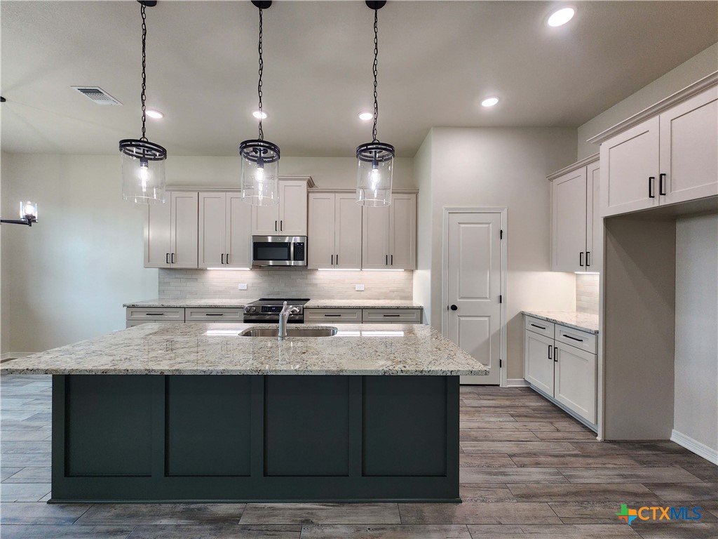 406 Talon Loop Salado, TX 76571 - Photo 7 of 31 a large kitchen with stainless steel appliances kitchen island granite countertop a stove a sink and a wooden floor