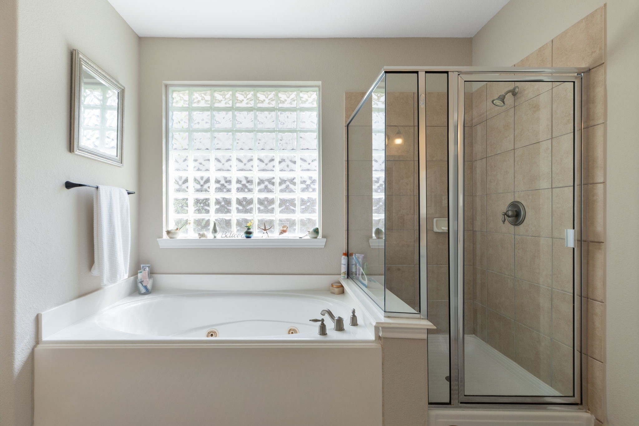 20410 Misty Crossing Lane Spring, TX 77379 - Photo 24 of 50 This spacious bathroom features dual sinks with black fixtures, a large mirror, a comfortable vanity area, and a soaking tub. The room is brightened by natural light from a glass block window, enhancing the clean, modern design with neutral tones.