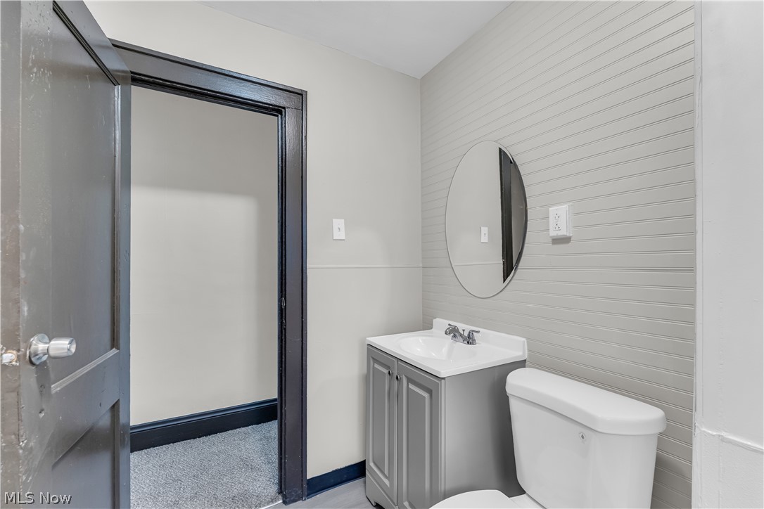 1144 East 145th Street, Unit 1/RIGHT Cleveland, OH 44110 - Photo 18 of 20 Bathroom featuring a compact vanity with a white countertop, an oval mirror, a standard toilet, and a textured accent wall