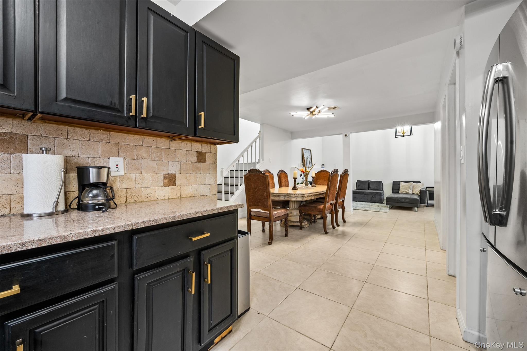 1016 Westwood Road Woodmere, NY 11598 - Photo 14 of 23 Kitchen with dark cabinetry, freestanding refrigerator, light stone counters, backsplash, and light tile patterned floors