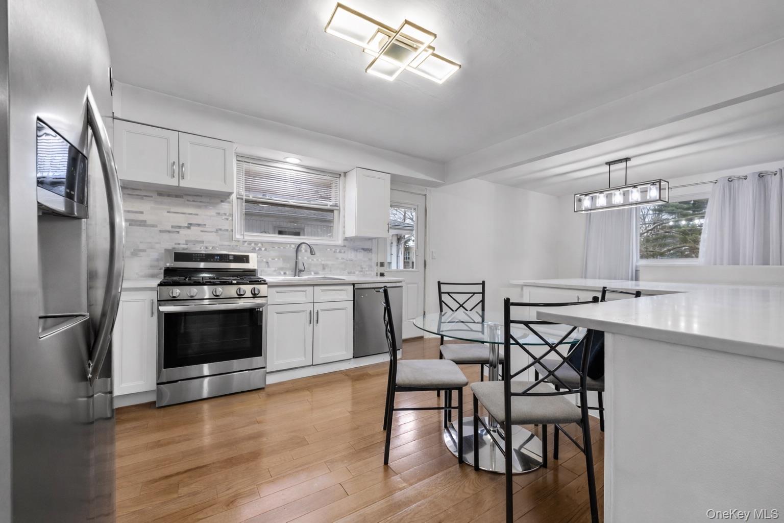 1016 Westwood Road Woodmere, NY 11598 - Photo 5 of 23 Kitchen featuring stainless steel appliances, white cabinets, light wood-type flooring, backsplash, and decorative light fixtures