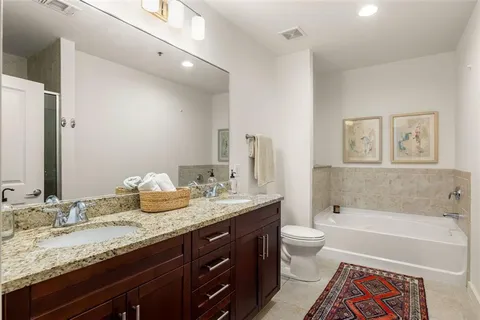 a bathroom with a granite countertop bathtub sink vanity mirror and toilet
