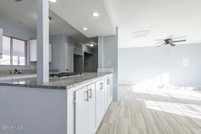 a view of an empty room and kitchen with wooden floor