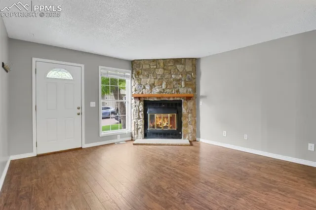 a view of an empty room with wooden floor fireplace and a window