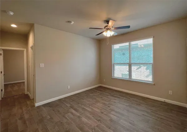 an empty room with wooden floor fan and windows