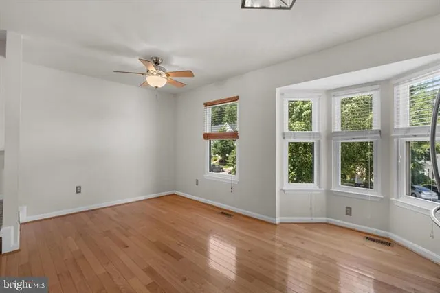 an empty room with wooden floor ceiling fan and windows