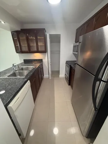 a kitchen with stainless steel appliances granite countertop a refrigerator a stove and a sink with wooden floors