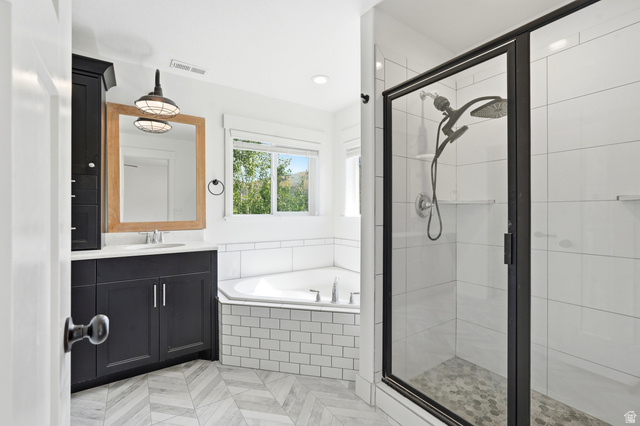 338 Windy Rdg Drive Smithfield, UT 84335 - Photo 35 of 63 Bathroom featuring a corner soaking tub, a stand-up shower with a glass enclosure, a single vanity with dark cabinetry and a light-colored countertop, a wood-framed mirror, and patterned tile flooring