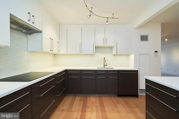 a kitchen with a sink dishwasher and white cabinets with wooden floor