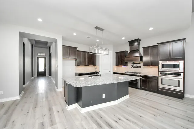 a large kitchen with stainless steel appliances kitchen island granite countertop a large counter top and stove top oven with wooden floor