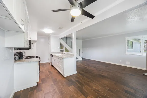 a kitchen with granite countertop a stove a sink and white cabinets with wooden floor next to windows