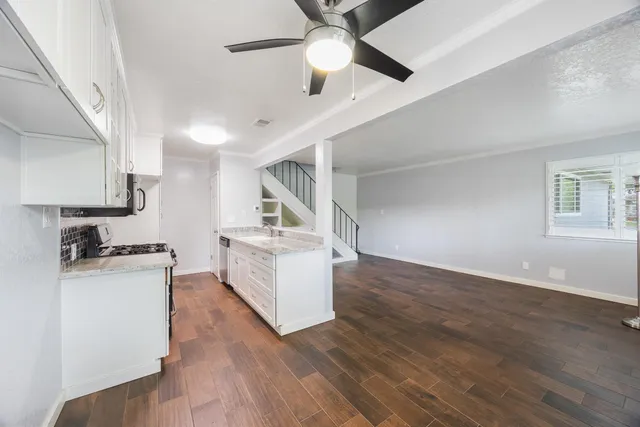 a kitchen with granite countertop a stove a sink and white cabinets with wooden floor next to windows