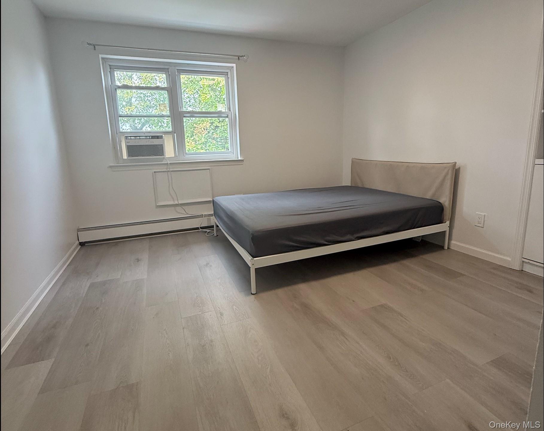 43-24 163rd Street Queens, NY 11358 - Photo 4 of 12 Bedroom featuring light wood-type flooring, a baseboard radiator, and cooling unit