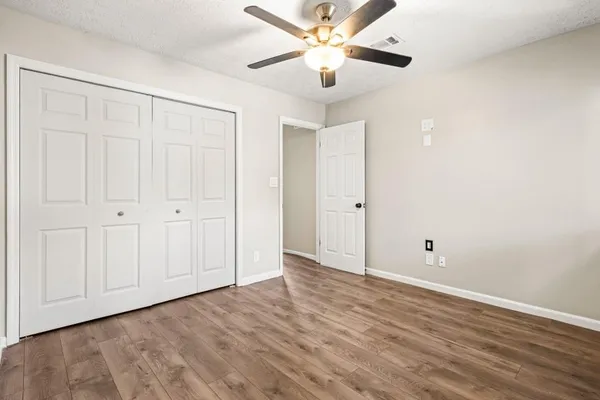 an empty room with wooden floor closet fan and windows