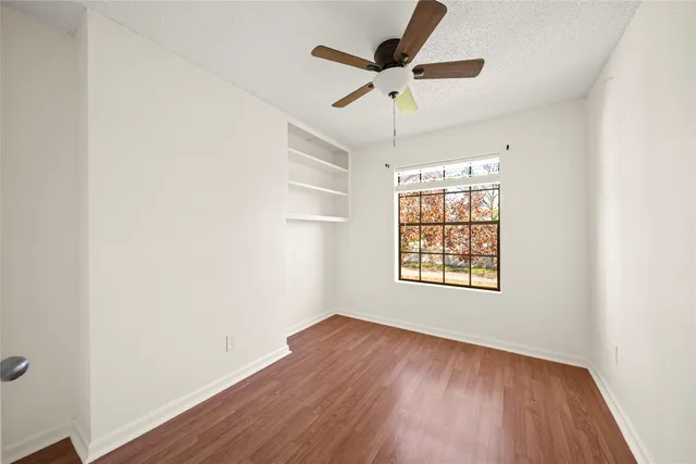 an empty room with wooden floor chandelier fan and windows