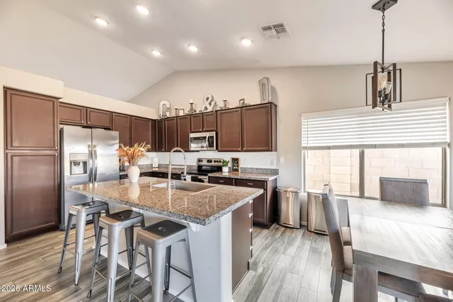a kitchen with granite countertop kitchen island stainless steel appliances a stove a refrigerator a sink a dining table and chairs with wooden floor