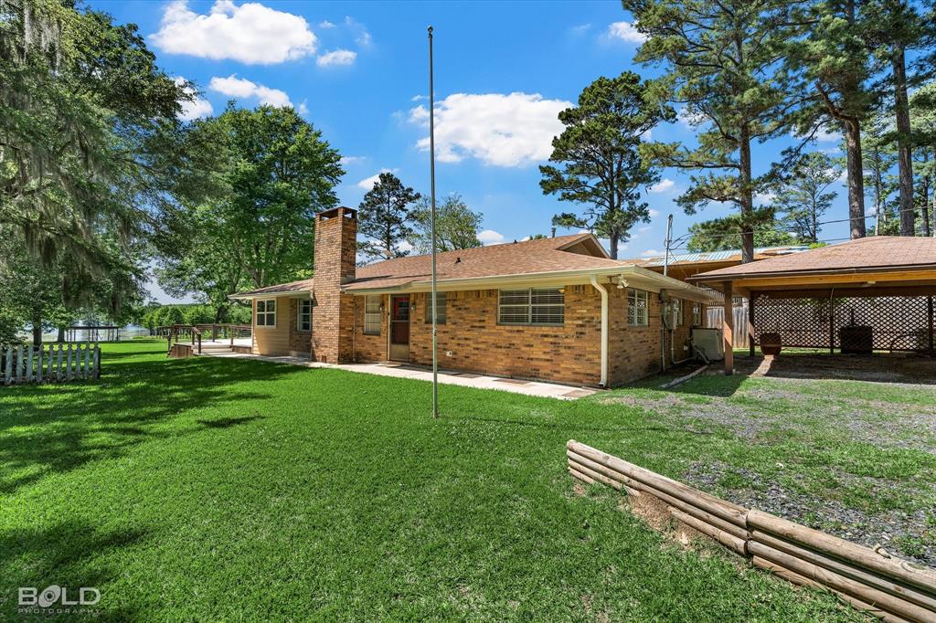 225 Marie Road Ringgold, LA 71068 - Photo 7 of 40 Brick exterior residence featuring an attached carport, prominent brick chimney, and a sprawling green lawn