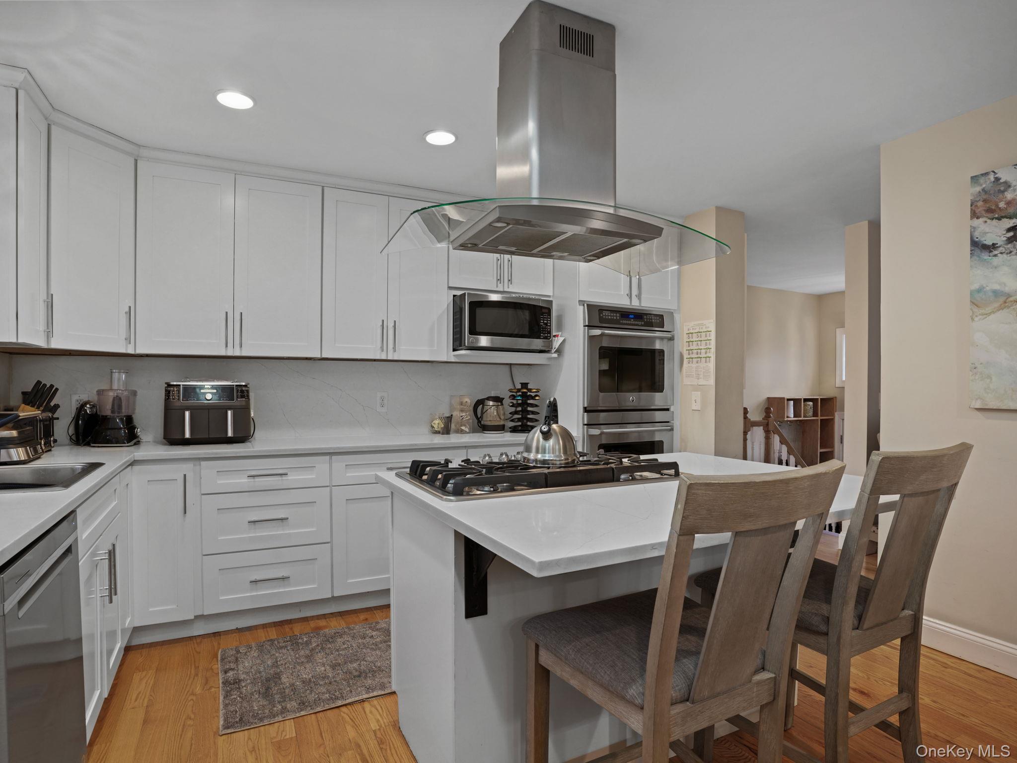 38 Kathwood Road White Plains, NY 10607 - Photo 15 of 44 Kitchen featuring island exhaust hood, decorative backsplash, white cabinets, stainless steel appliances, and a breakfast bar