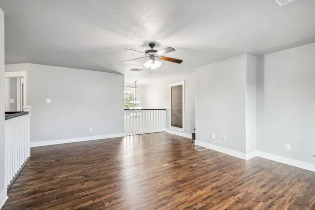 a view of an empty room with wooden floor and a ceiling fan