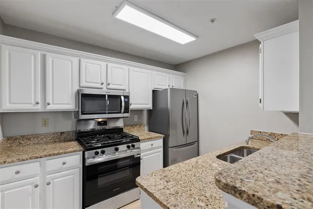 a kitchen with granite countertop a refrigerator stove and white cabinets