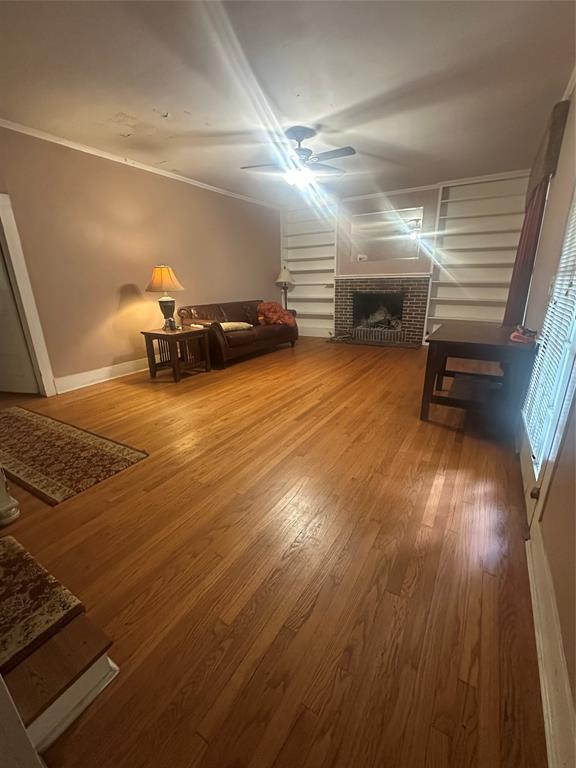 504 1st Street Terrell, TX 75160 - Photo 10 of 27 Living area featuring wood-finish flooring, a brick fireplace, built-in shelving, a ceiling fan, and crown molding