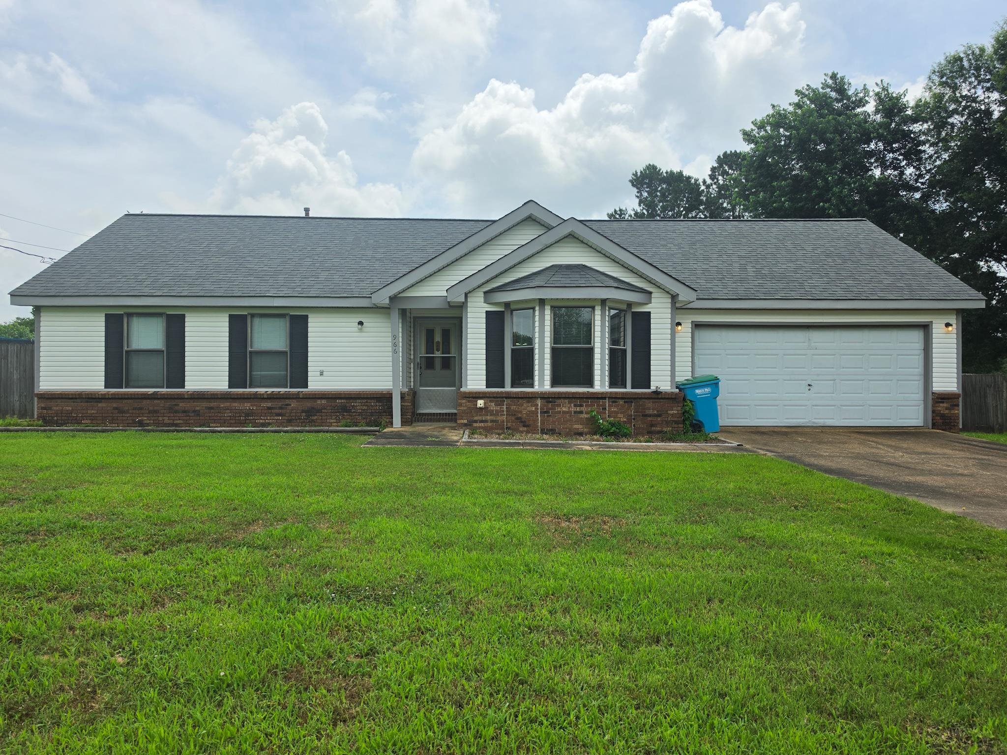 Single-story residence featuring a gray shingle roof, white siding, and a brick skirt