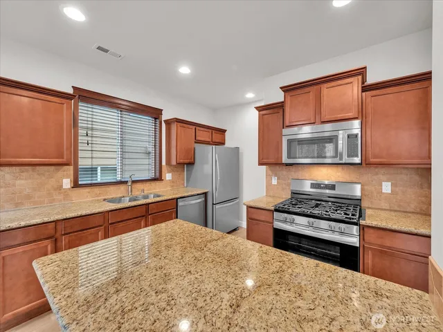 a kitchen with stainless steel appliances kitchen island granite countertop a stove and a refrigerator