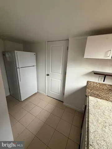 a view of a refrigerator in kitchen and an empty room