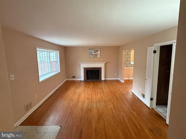 an empty room with wooden floor fireplace and windows