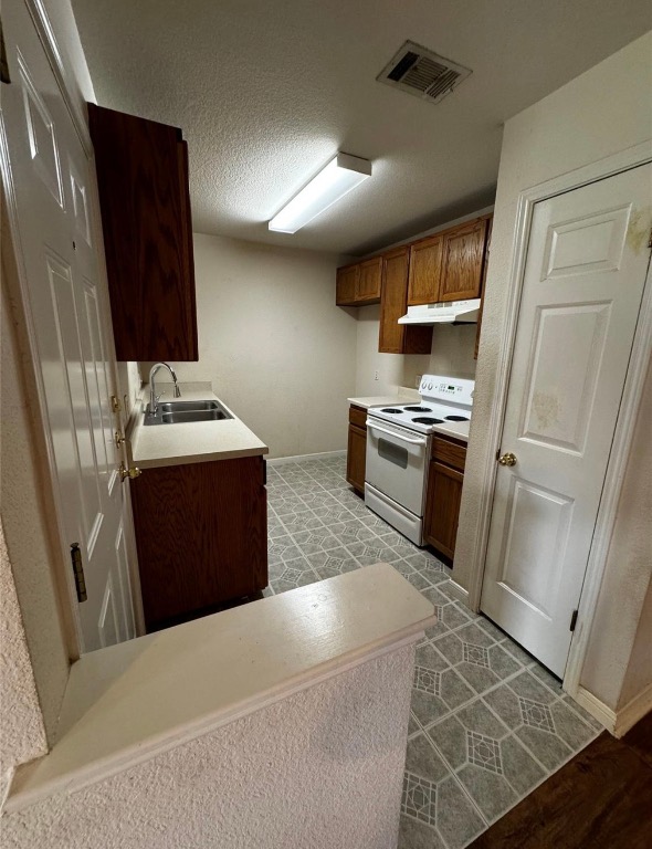 8613 Talyne Chaise Circle Austin, TX 78729 - Photo 4 of 22 Kitchen featuring white electric range oven, light countertops, a textured ceiling, under cabinet range hood, and brown cabinetry